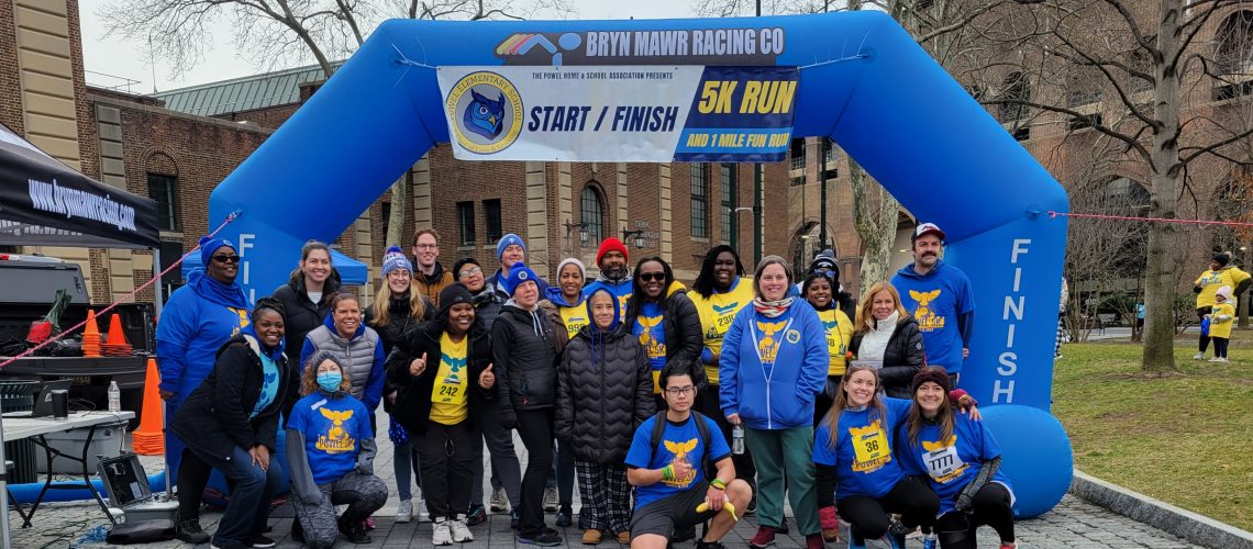 Powel Staff and Volunteers under blue, inflatable arch at the inaugural 5K in March 2023